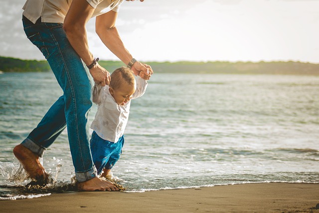 Father teaching toddler to walk along the shore, supporting primary care for all ages