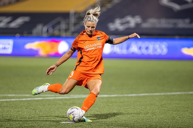 Female football player in an orange jersey playing on a field during a student physical examination